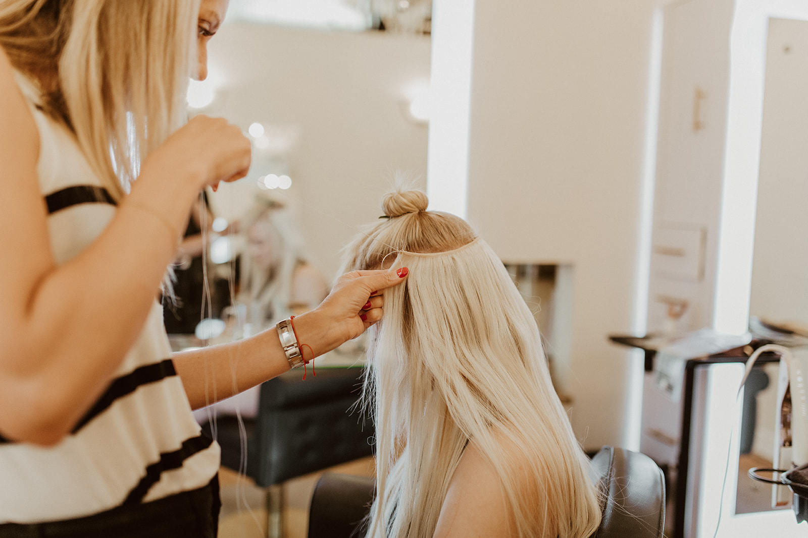 Stylist installing hand-tied extensions on a blonde client at Fluff